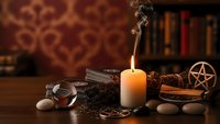 Mystical altar setup with burning candle, crystals, pentagram, dried herbs and ritual tools on wooden table creating atmospheric spiritual workspace.
