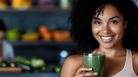 Young African American woman with curly hair smiling while holding fresh green smoothie in kitchen, healthy lifestyle and wellness concept for nutrition blogs.