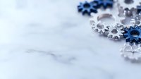 Silver and blue metallic gears scattered on white marble surface with selective focus creating depth and modern industrial composition for business concepts.