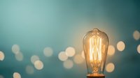 Vintage Edison light bulb glowing warmly against soft teal background with bokeh lights creating atmospheric ambiance for creative inspiration concepts.