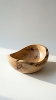 Hand-turned wooden bowl with natural knots and organic grain texture, crafted from light hardwood, displayed on a white surface in soft sunlight.