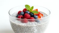 Chia seed pudding topped with fresh raspberries, blueberries, strawberries, and mint in a glass bowl on white background.