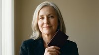 Confident mature Caucasian businesswoman with gray hair in professional black blazer smiling warmly in modern office setting for corporate leadership concepts.