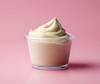 Creamy soft serve vanilla yogurt or ice cream swirl in clear glass cup against pink background, minimalist food photography style for dessert menu or advertising.