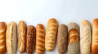 Assortment of freshly baked bread loaves arranged in row showing variety of crusts, textures and baking styles for bakery or food industry use.