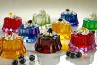Colorful gelatin desserts topped with whipped cream and fresh berries arranged on white surface, perfect for food photography, recipe blogs, and culinary design projects.