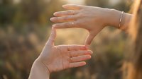 Female hands forming frame gesture in golden sunlight capturing moment with fingers creating viewfinder shape for photography composition and creative vision.