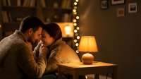 Romantic couple embracing intimately in cozy living room with warm lighting and fairy lights creating perfect atmosphere for love and togetherness at home.
