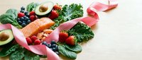 Fresh salmon fillet with colorful vegetables, berries and pink ribbon on wooden background. Healthy eating concept for cancer awareness campaigns.
