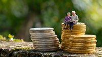 Senior couple figurines sitting on stacked coins representing retirement planning and financial security for elderly people in golden years.