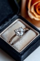 Heart-shaped diamond engagement ring in platinum setting displayed in black velvet jewelry box with soft rose in background, romantic proposal concept.