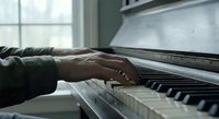 Close-up of hands playing piano keys in cozy home interior with natural window light creating peaceful musical atmosphere for relaxation and practice.