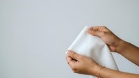 Close-up of hands holding and stretching white fabric or cloth material against neutral background for textile, design, and product mockup applications.