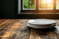 Stack of white ceramic plates on rustic wooden table near window with warm sunlight, creating cozy atmosphere for food photography and restaurant menu design.