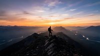 Silhouette of hiker standing on mountain peak at sunset with valley below, golden sky and distant mountains, outdoor adventure and achievement concept.