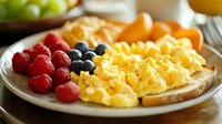 Fluffy scrambled eggs served on toast with fresh berries and fruit on white plate, morning breakfast setting with natural lighting and selective focus.