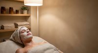Young woman relaxing with facial mask during spa treatment at home, enjoying skincare routine and wellness self-care moment in cozy bedroom setting.