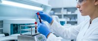 Female scientist in protective eyewear and blue gloves conducting laboratory research with pipette in modern medical facility for scientific analysis.