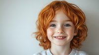 Happy redhead child with curly hair smiling at camera against white background. Portrait of cheerful young kid with freckles and bright ginger curls.