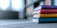 Stack of colorful hardcover books with vibrant spines in purple, red, yellow and teal arranged on light surface against blurred background, creating minimalist composition.