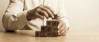 Businessman arranging wooden blocks with business icons in staircase formation, symbolizing strategy, growth, and step-by-step success planning.