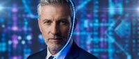 Senior male professional with gray hair and beard wearing dark business suit and blue shirt against digital technology background with glowing data streams and circuit patterns, representing cybersecurity, innovation, and corporate leadership.