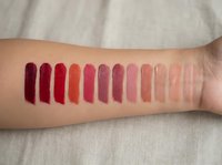 Lipstick color swatches on woman's arm showing gradient from deep burgundy to nude pink shades for cosmetic testing and beauty product comparison.