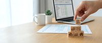 Business analytics concept with wooden cubes showing data charts and graphs on office desk with laptop displaying financial spreadsheet for strategic planning.