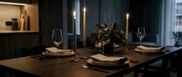Elegant dinner table setting with dark wood surface, gold candlesticks, wine glasses, and floral centerpiece for fine dining and event planning.