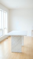 Modern white marble dining table with geometric base on hardwood floor in bright minimalist room with large windows for contemporary interior design.