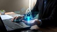 Businessman in suit holding glowing rocket hologram above laptop, symbolizing startup launch, innovation, and digital business growth.