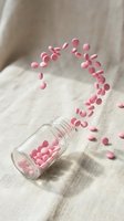 Pink pills spilling from glass bottle in dynamic motion on neutral fabric background for healthcare and pharmaceutical concepts.