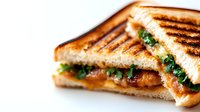 Grilled sandwich with melted cheese, crispy toasted bread, and fresh green lettuce leaves on white background, close-up view showing texture and layers.