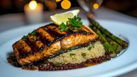 Grilled salmon fillet with grill marks served on quinoa, garnished with fresh parsley, lime wedge and grilled asparagus spears in romantic candlelit setting.