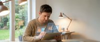 Young Caucasian man using tablet computer at home office desk with warm lighting for remote work and digital technology applications.