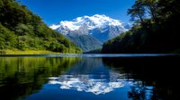 Tranquil mountain lake reflects snow-capped peaks and lush forest under vibrant blue sky, creating mirror-like symmetry in pristine wilderness landscape.