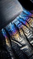 Iridescent bismuth crystal formation displaying rainbow metallic colors and geometric stepped structure in macro photography for science and technology concepts.
