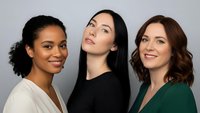 Three diverse professional women smiling confidently in business attire against neutral background for corporate marketing and teamwork concepts.