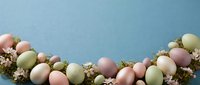 Pastel colored Easter eggs in soft pink green and cream tones arranged with dried flowers on blue background for spring holiday decorations.