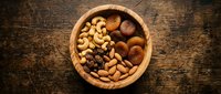 Mixed nuts and dried fruits in wooden bowl on rustic table for healthy snacking and cooking ingredients.