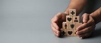 Hands protecting wooden blocks with healthcare and insurance symbols including medical cross, heart, and shield icons for coverage concepts.