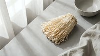 Dried enoki mushrooms bundle placed on neutral linen fabric with ceramic bowl and natural light, suitable for food styling and culinary content.
