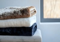 Stack of folded soft plush blankets in neutral colors brown, white and navy blue on light background, cozy home textile arrangement for interior decor.