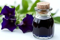 Dark liquid in small glass bottle with cork stopper next to vibrant purple flowers against soft green background, selective focus on bottle for spa and wellness.