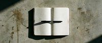 Open notebook with grid pages and black pen casting shadow on concrete surface for creative writing and planning projects.