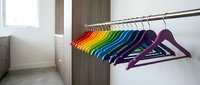 Colorful rainbow hangers arranged on closet rod in modern wardrobe interior for clothing organization and storage solutions.