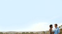 Young couple enjoying outdoor romantic moment in countryside landscape with rolling hills and natural scenery, suitable for relationship, lifestyle, and travel marketing materials.
