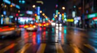 Blurred city street at night with colorful bokeh lights reflecting on wet pavement creating abstract urban atmosphere for backgrounds and design projects.
