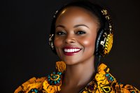 Young African woman wearing traditional colorful dress and decorative headphones smiles radiantly against dark background, expressing joy and cultural fusion.