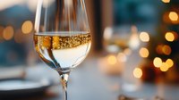 Sparkling white wine in elegant glass with golden bokeh lights in background creating romantic festive atmosphere for celebration or special occasion.